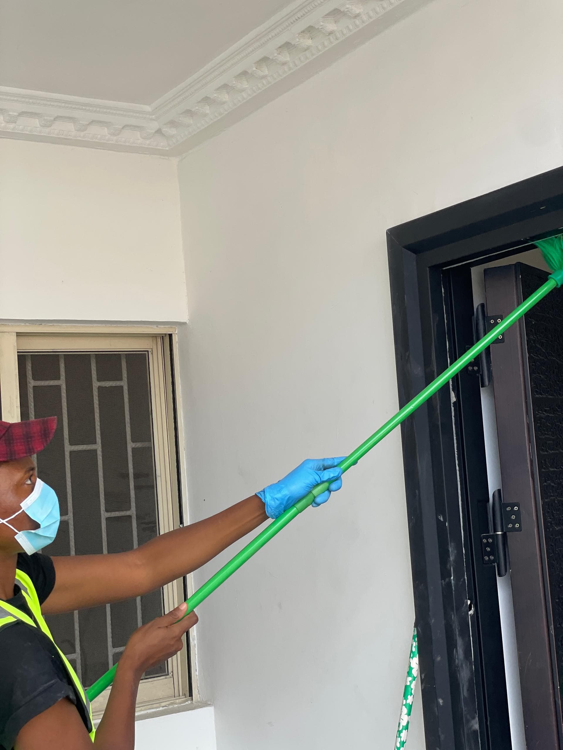 Etanaya operative using an extendable duster to clean high interior cornice work