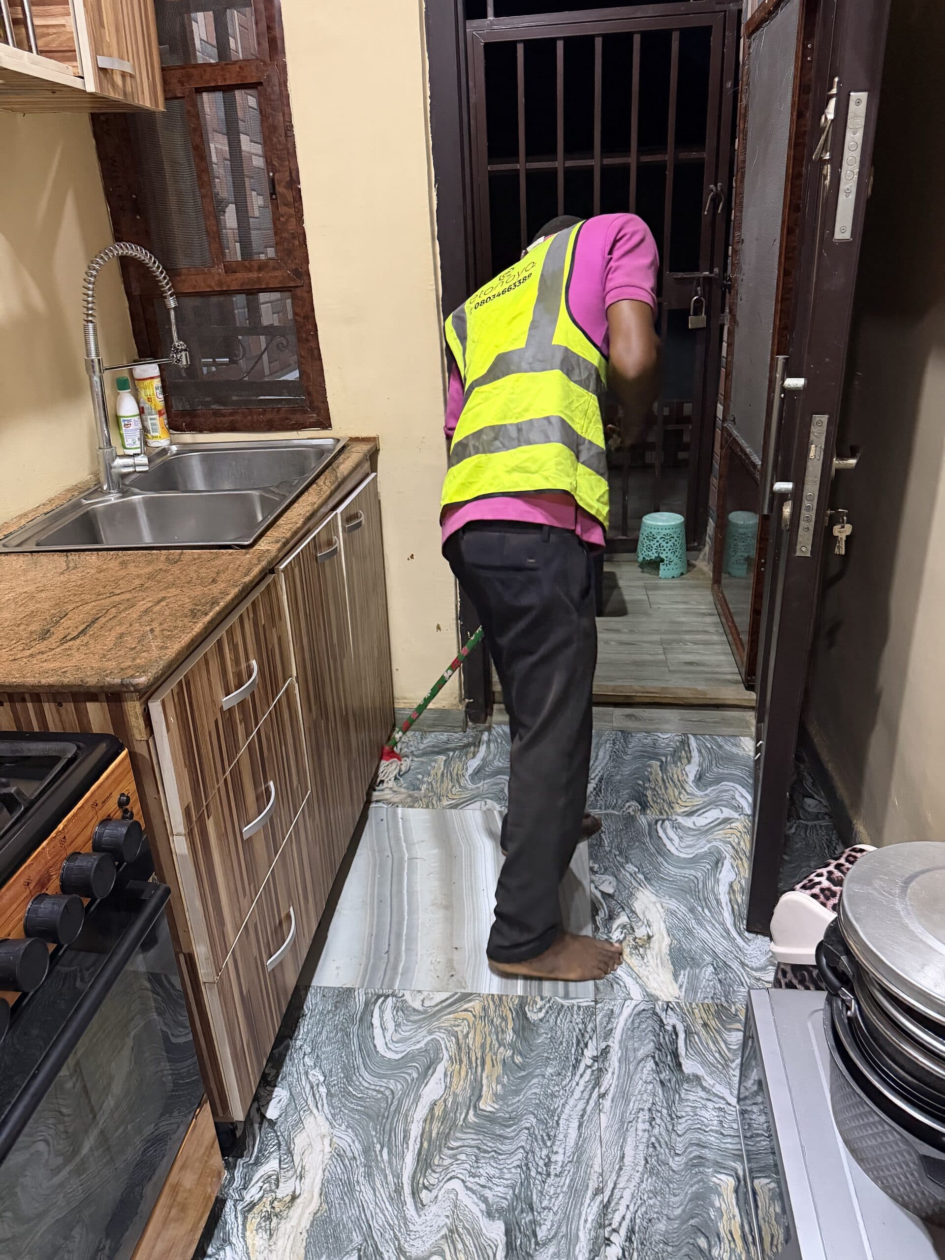 Operative in branded hi-vis mopping a kitchen floor with cleaning kit alongside