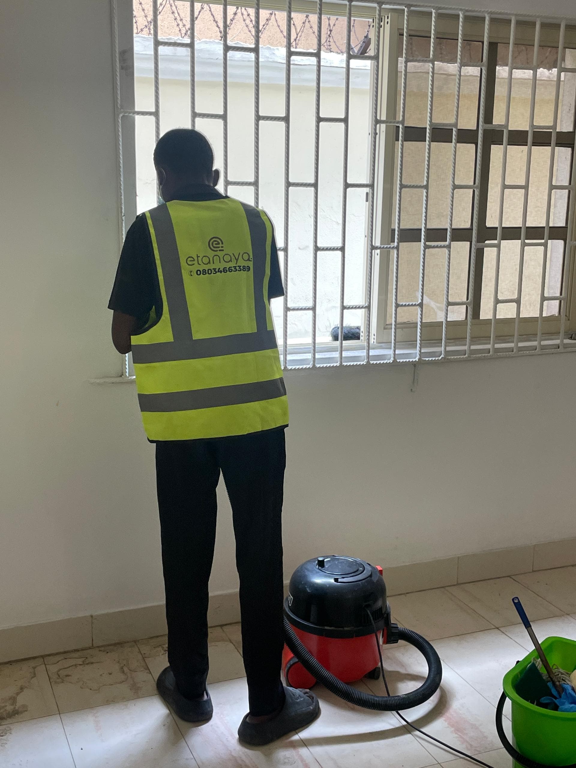 Etanaya operative in branded hi-vis cleaning a window frame, with commercial vacuum and mop bucket alongside
