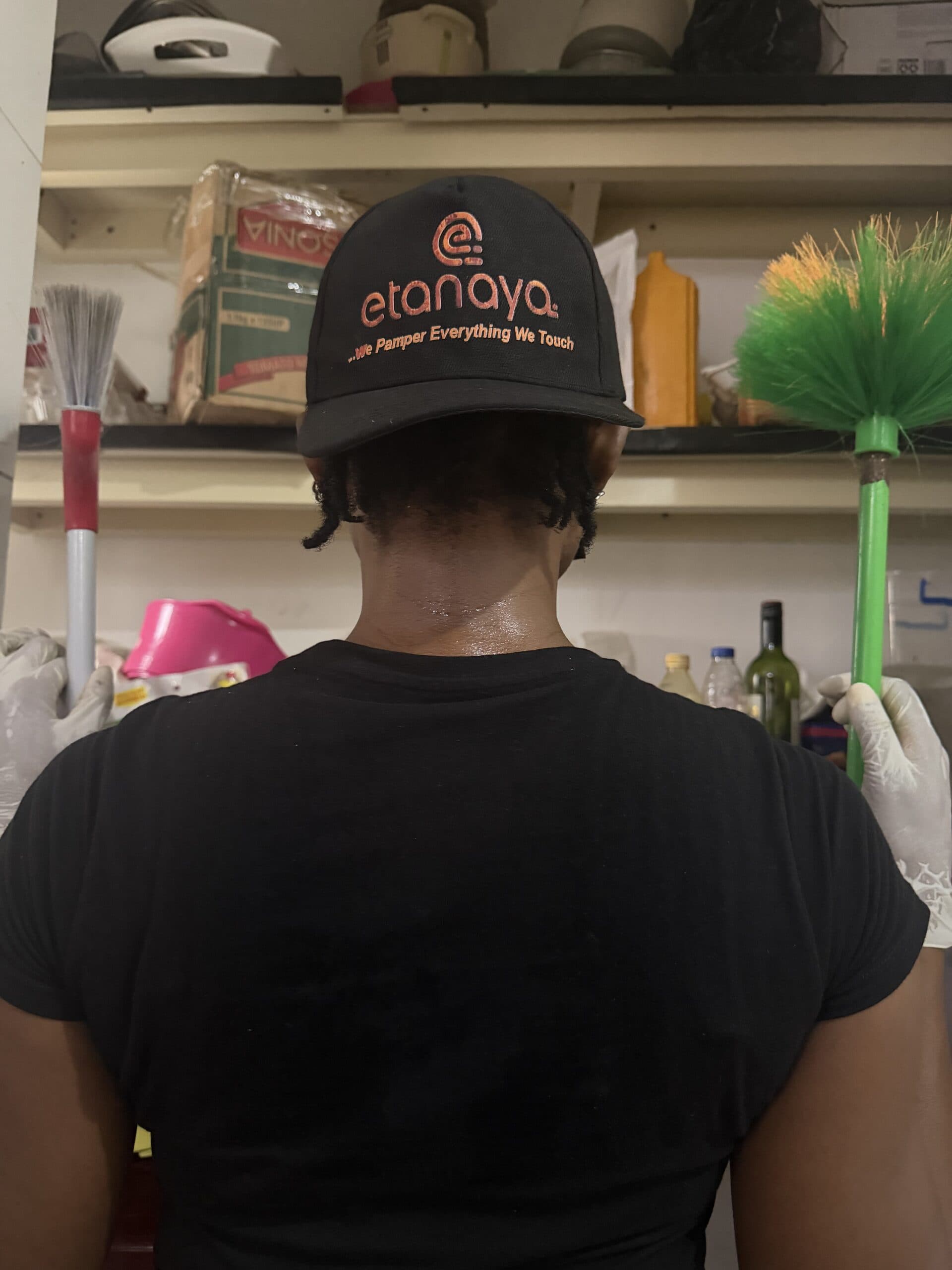 Etanaya operative in a branded cap, seen from behind, with brushes and cleaning tools on the shelf ahead